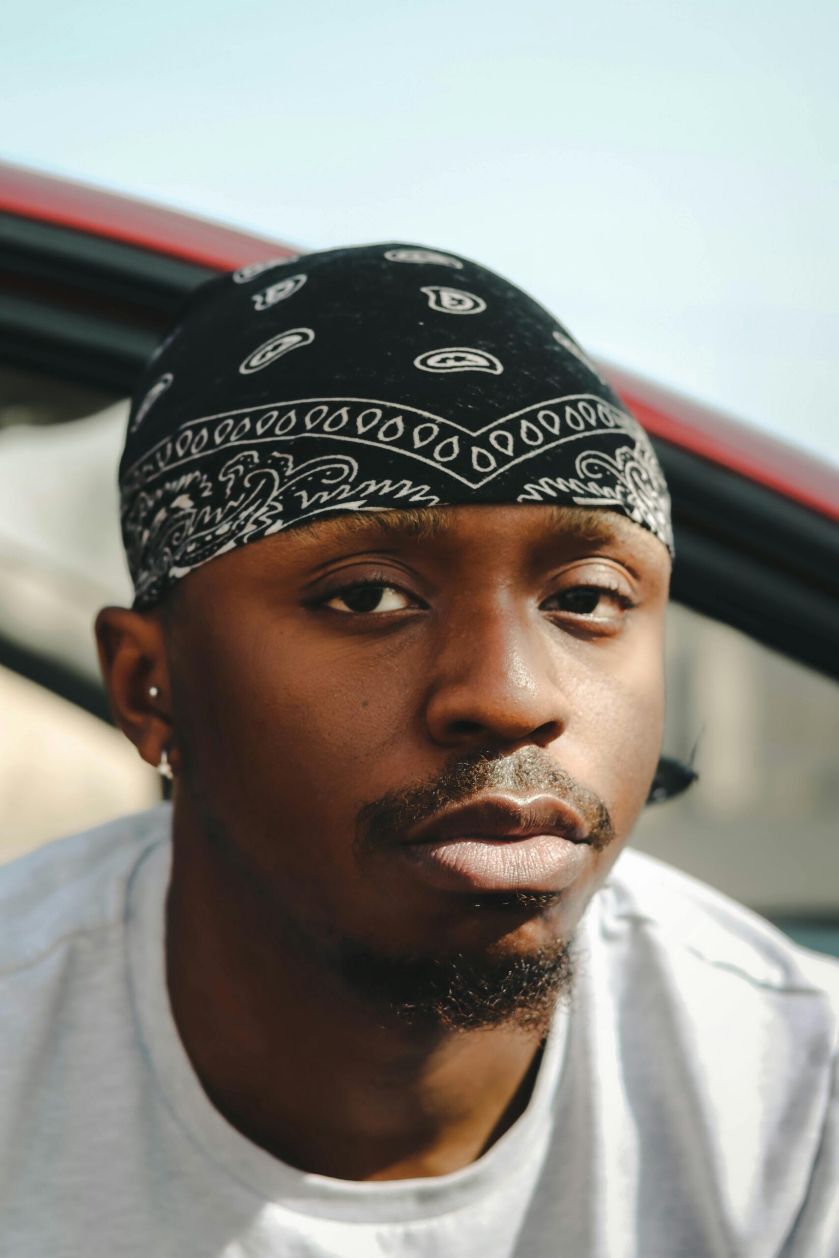 Close-up portrait of a man wearing a bandana sitting in a car on a sunny day.
